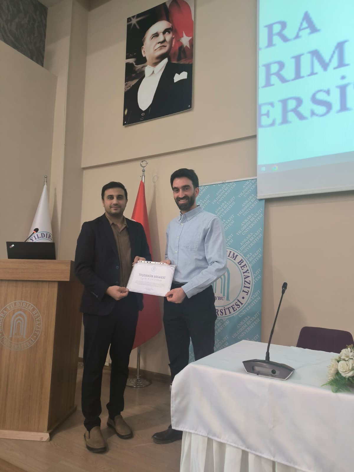 Makine Mühendisliği Bölüm Başkanı Profesör Doktor Selahattin Çelik bölüm öğretim üyelerinden Doktor Mahmut Cihat Yılmaz'a teşekkür belgesi veriyorken çekilmiş fotoğraf.